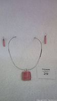Sterling silver necklace with square pink stone pendant and matching pink enamel earrings laid out on white background.