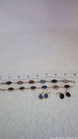 Full lot view: two multi-gemstone scarab bracelets laid next to a ruler and two pairs of scarab gemstone earrings.