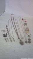 Overview photo showing multiple pieces of silver jewelry including necklaces, earrings, pendants, and pins laid out on cloth