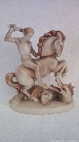 Front angle of the Hummel St. George and the Dragon porcelain figurine showing the mounted figure raising a sword above a dragon at the horse's feet.