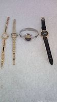 Four vintage watches laid out: Movado with leather strap, Seiko metal bracelet, Tradition cuff style, LaFon stone-adorned band.