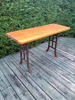 Console table showing the full length and height with cast iron ends and solid pine plank top on outdoor decking.