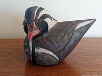 Front and side view of colorful ceramic wood duck figurine with detailed stylized feather painted design and red beak.