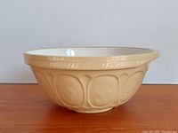 Side view of beige Gresley stoneware mixing bowl with embossed oval relief and smooth white glazed interior.