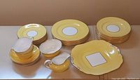 View of entire luncheon set showing plates, cups, cream jug, sugar bowl, and serving platter with yellow and gold detailing.