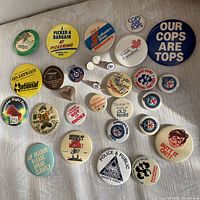 Full assortment of enamel pins and buttons laid out on white fabric, showing variety in size, color, and design.