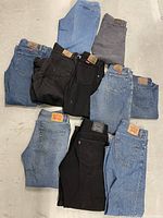 Photo showing 10 pairs of denim jeans arranged on floor with visible Levi's, Lee, and Wrangler branding.