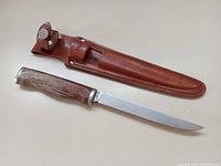 Fish fillet knife laid next to its brown leather sheath on a flat surface.