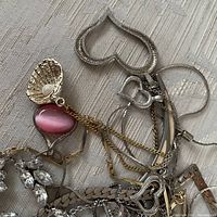Mixed assortment of jewelry pieces tangled together including 925 silver bangle, heart-shaped pendant, faux pearl shell pendant, pink cabochon pendant, and rhinestone earrings.