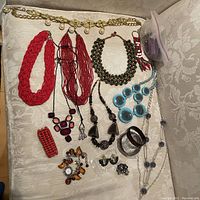 Overview photo showing the chain belt with dangling faux pearls, various beaded necklaces in red, black, and blue colors, multiple bracelets including the watch with amber beads, flower ring, and other assorted rings and earrings.
