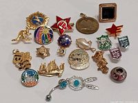 Top-down view of 18 assorted vintage pins and pendants, showing designs, colors and overall layout.