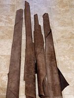 Four rolled chocolate brown leather hides arranged vertically on a tiled floor, showing their length and condition.