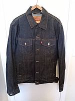 Front view of dark blue Levi's denim jacket hanging on a hanger, showing button front and chest pockets with Levi's signature red tab.