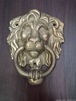 Front view of the vintage brass lion's head door knocker mounted on a wooden surface.