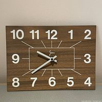 Full view of the rectangular mid-century modern wall clock with wood grain background, white numbers and hands.