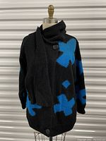Front view showing black mohair sweater with large blue crosses, attached black scarf wrapped around collar, and top and bottom large buttons visible.
