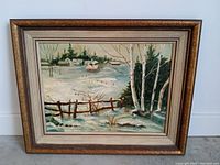 Framed vintage oil painting showing a snowy winter landscape with birch trees and rustic fences.