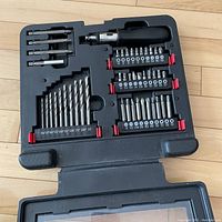 Open case showing the screwdriver handle, two rows of screwdriver bits, and drill bits arranged neatly in a molded plastic case.