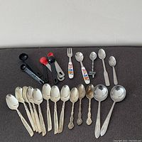 Overview of vintage silverplate teaspoons, measuring spoons and souvenir spoons on dark fabric