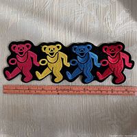 Top view of the embroidered iron-on patch featuring four dancing bears in pink, yellow, blue, and red, with measuring tape showing approximately 10 inches length.