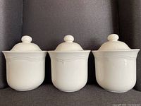 Three large vintage white ceramic canisters with lids arranged in a row showing overall shape and size.