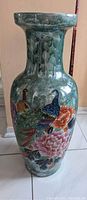 Front view of a large vintage ceramic vase with detailed peacock and flower designs in vibrant colors and a green mottled background.