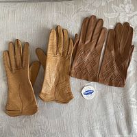 Two pairs of small ladies leather gloves laid flat on a patterned fabric surface, showing front and back details.