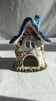 Front view of the ceramic tealight house showing the arched door opening, window with grids and floral decorations on the walls and base.