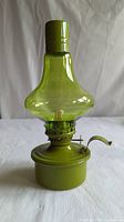Front view of green glass oil lamp showing bulbous chimney and metal base with wick adjustment knob.