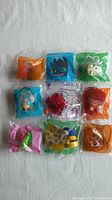 Overview of all nine McDonalds Happy Meal toys individually sealed in original plastic bags in various colors including orange, blue, green, pink, and clear. Toys appear to be character figures designed for children's play or collectibles.