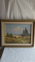 Framed oil painting showing entire meadow landscape with trees, path, and distant hills.