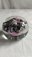 Front view of glass paperweight showing pink and black swirls with bubbles inside clear glass.