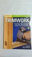 Front cover of the book titled 'Ultimate Guide Trimwork' showing a hand using a nail gun on wood trim.