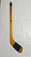 Full wooden mini hockey stick showing the blade with black tape and the length with Maple Leafs logo and autographs stamped on the wood.