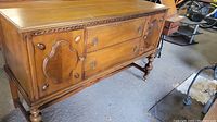 Front angle view of the wooden buffet showing two doors with carved panels and two drawers with keyhole hardware.