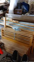 Wooden slatted bed frames stacked with metal rails and hardware bags in a pile