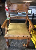 Front view of a carved oak armchair showing decorative backrest, leather seat with nailhead trim, and claw-foot legs.
