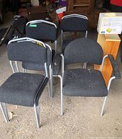 Photo showing four chairs from set, three standard desk chairs and one armchair with metal armrests, all with gray metal frames and dark gray upholstery.