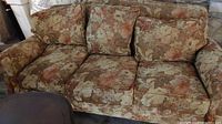 Front angle showing full view of three-seat overstuffed floral couch with visible wear and fraying on upholstery.