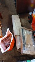 The flooring offcut piece lying on the floor alongside the two unopened Ikea Rationell drawers in plastic packaging and an open orange bag nearby.