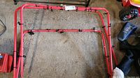 Folded red metal frame with black elastic netting laid on concrete floor, showing hooks securing the net to frame.