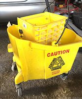 Yellow Rubbermaid mop bucket with wringer and four swivel casters, caution hazard sign visible on the side, showing side and angled views.