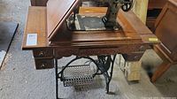 Side view of antique sewing machine with wooden cabinet and treadle mechanism