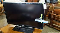 Front view of the 42 inch Sharp Aquos TV showing the screen and base stand with remote attached.