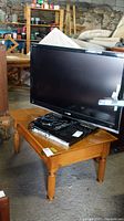 Wood table with a TV and other electronics on top, showing the tabletop and legs.