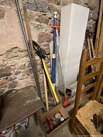 Photo showing multiple garden tools including a crowbar, electric weed snipper, garden edger, Polaris spa wand, ground tamper and other assorted tools in front of a stone wall.