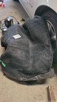 Folded black trampoline safety netting shown on a floor next to a vehicle wheel.