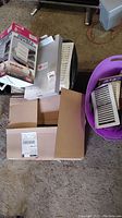 Several white plastic vent covers and some vent cover boxes on the floor near a metal filing cabinet extension in a partially open box.