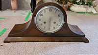 Side view of the wooden mantel clock showing curved top and wooden base with clock face visible