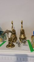 Photo showing two tall brass elephant figurines with elongated necks and a brass elephant holding an umbrella alongside two small silver-toned metal elephants.
